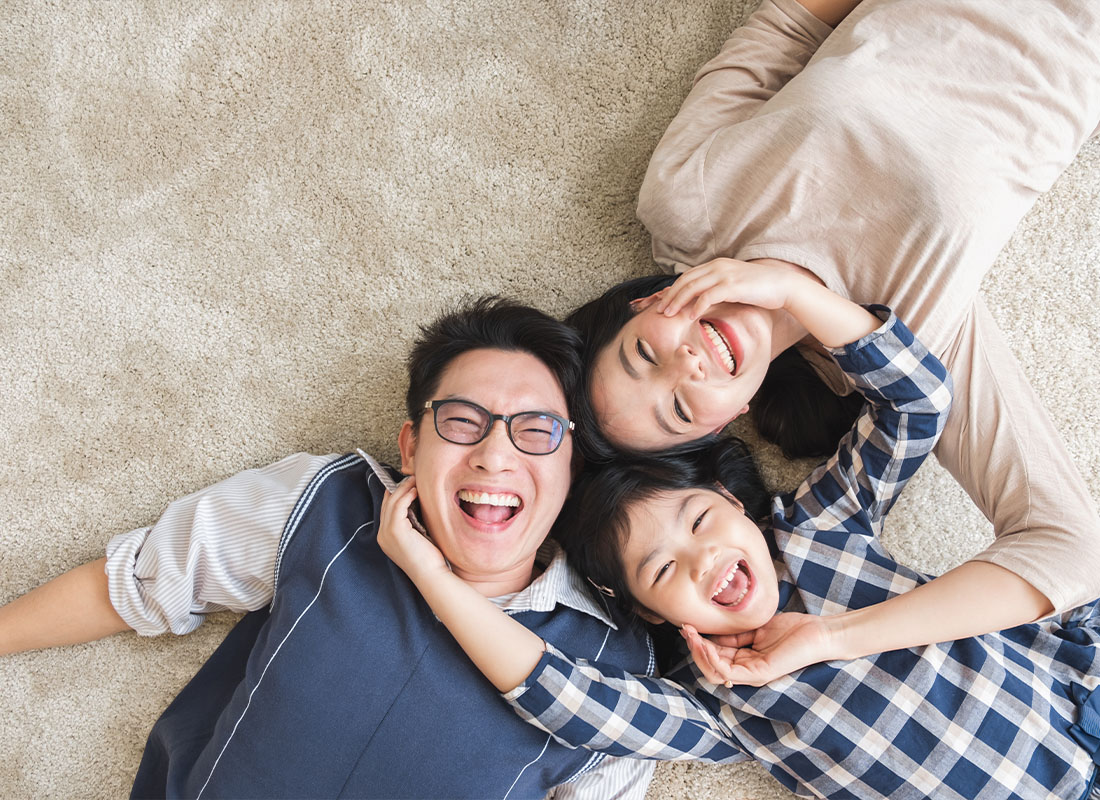 Insurance Solutions - A Happy Family Laying Together on the Carpet Floor With Smiles on Their Faces